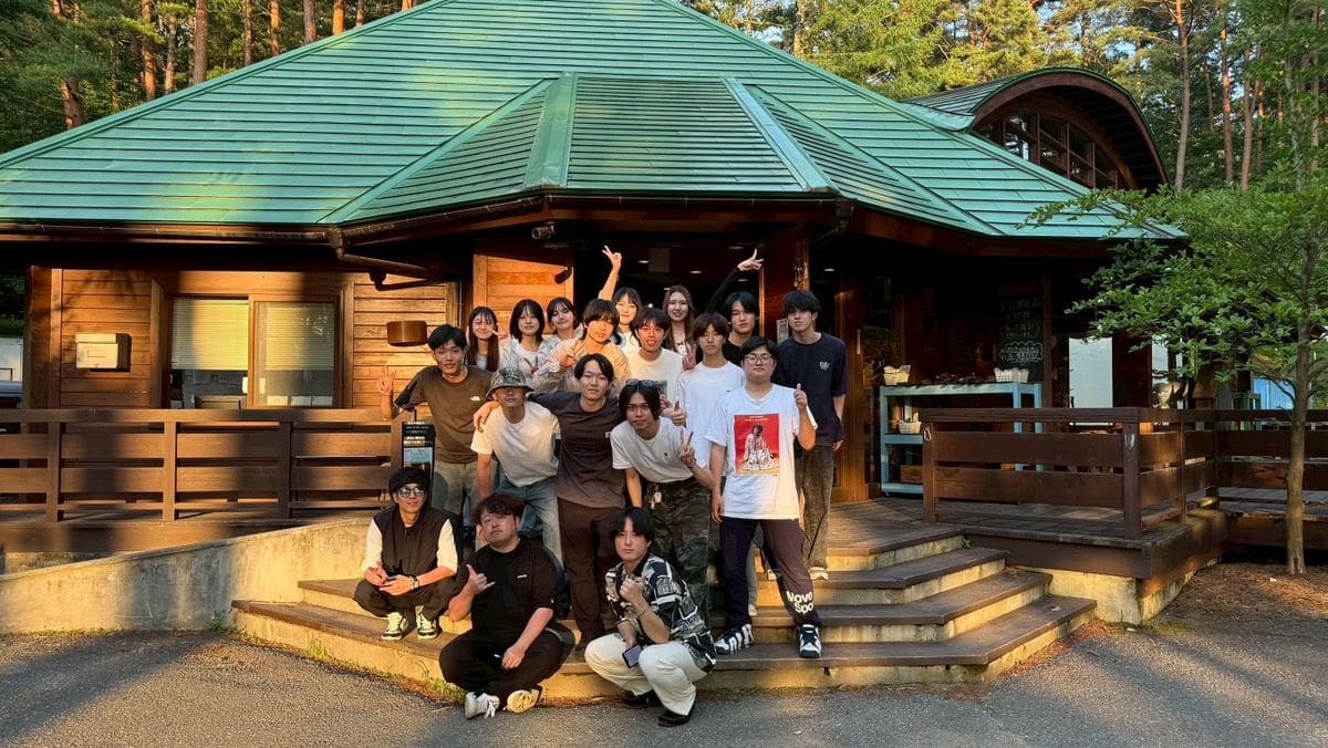 夕方の光の中、緑の屋根の木造の建物の前の階段に、たくさんの人が集まって並ぶ集合写真