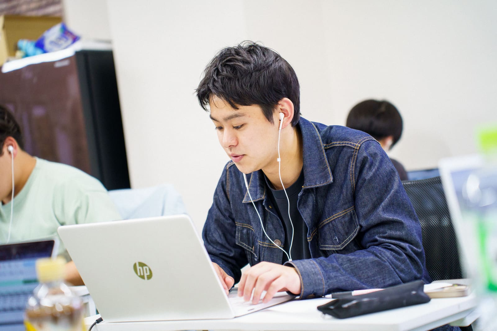 デニムジャケットの男性が、イヤホンをつけて、ノートPCの画面に集中している
