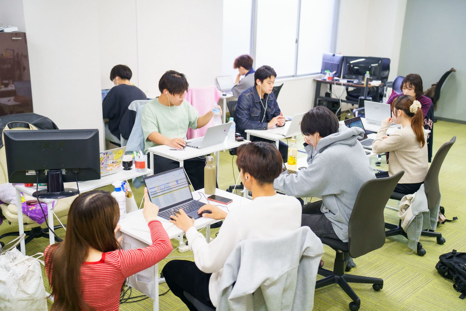 窓から光が入るオフィスで、机を囲んで、メンバーたちがそれぞれノートPCに向かっている