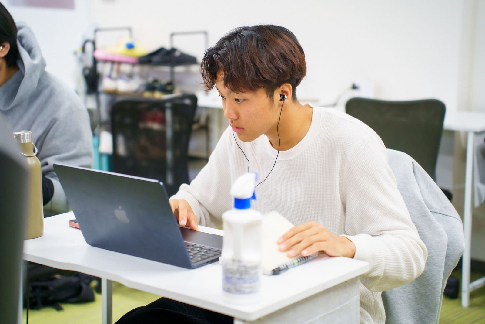 白いニットの男性が、イヤホンをつけて、身を乗り出すようにノートPCの画面を見ている