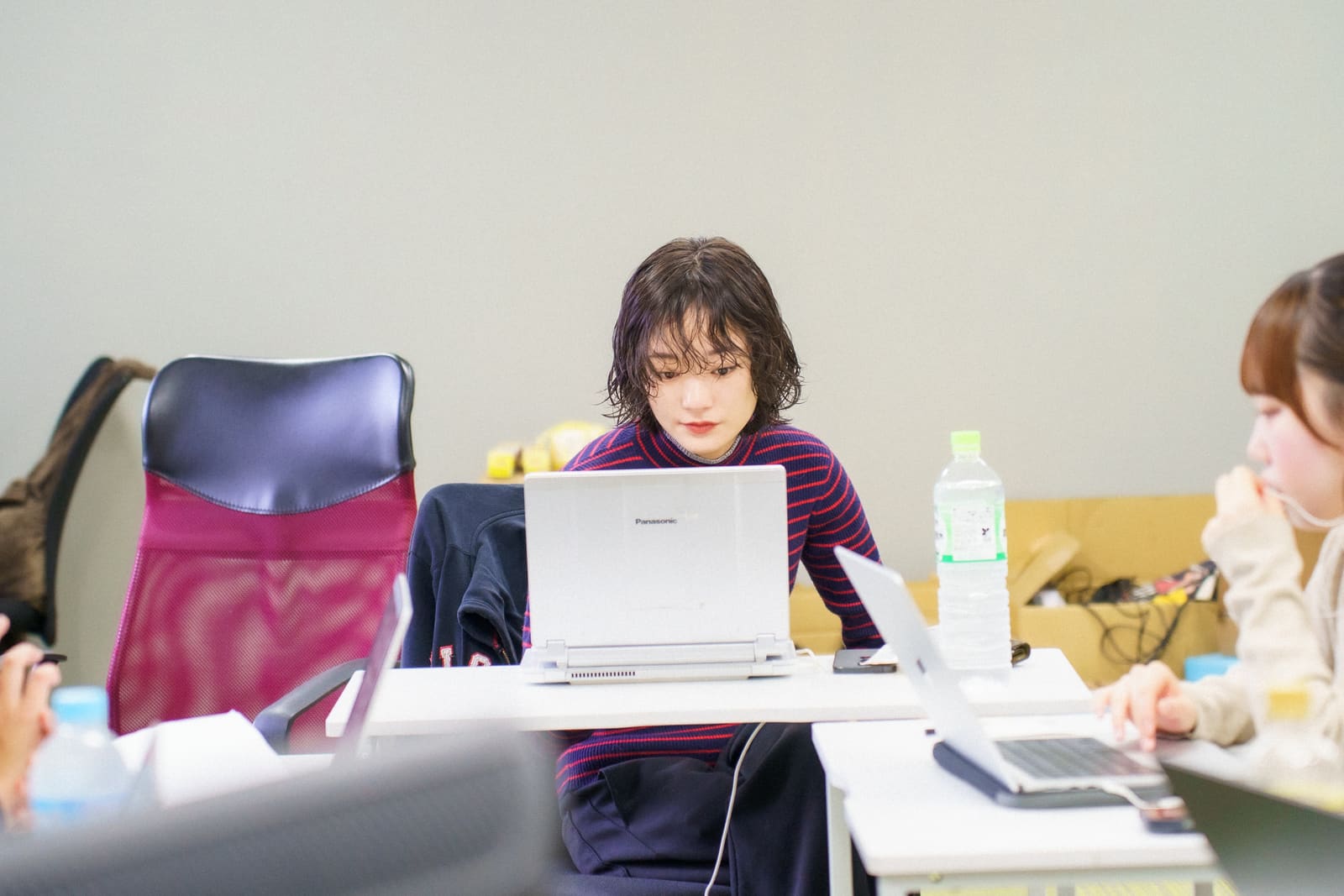 ウェーブのかかった短い髪の人が、紫のボーダーの服で、白いノートPCに向かっている