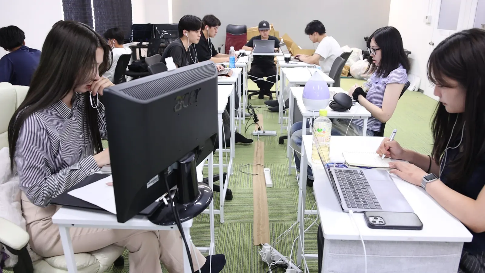 長い机が2列で奥まで並ぶオフィスで、10人ほどのメンバーが、それぞれノートPCやモニターに向かって作業している