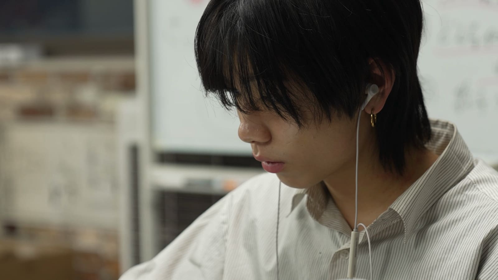 イヤホンをつけた黒髪の男性が、うつむいて画面を見ている