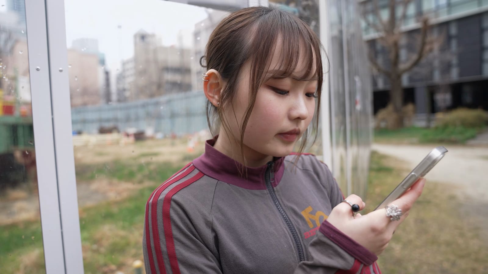 公園で、赤い線の入ったジャージの女性が、うつむいてスマートフォンを見ている