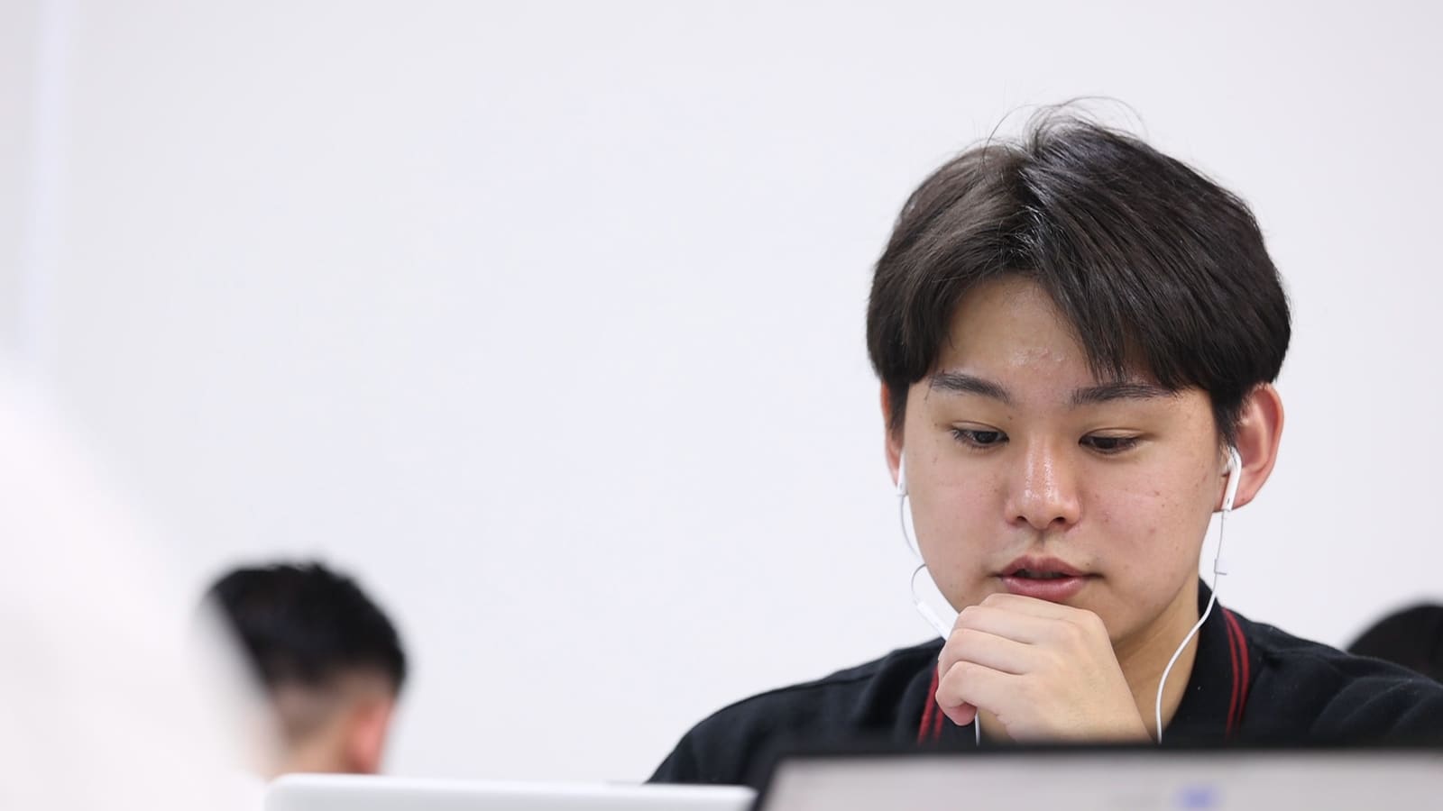 黒いポロシャツの男性が、イヤホンをつけて、口元に手を当てて画面を見ている
